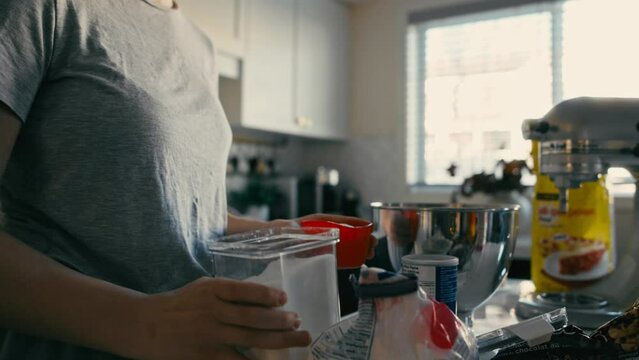 A woman measures and pours sugar into a  metal mixing bowl in a handheld slow-motion shot, featuring a slight push-in as she pours. Great for baking tutorials, culinary vlogs or food-related content, 
