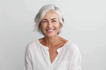 Portrait of a happy senior woman smiling at the camera while standing against grey background - obrazy, fototapety, plakaty