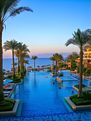 Bustling Resort Pool with Palm Trees at Sunset. Tropical resort natural pool.Travel concept