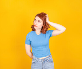 Confused young woman, close up portrait of caucasian confused young woman. She scratches her head thoughtfully. Looking aside. Yellow background, copy space. Don't know what to do concept idea image.