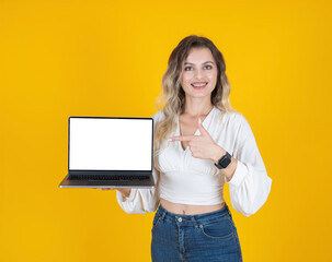 Laptop mock up, young caucasian woman holding empty screen laptop mock up. Standing over yellow studio background. Pointing index finger to notebook display. Smiling woman with braces. Copy space.
