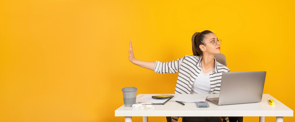 Stop palm gesture, young strict businesswoman employee sit office desk with laptop do stop palm gesture aside to copy space. Yellow studio background. Say no, refuse concept image. 