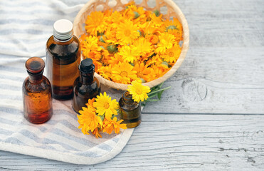 glass bottles with essential oil of calendula and fresh calendula flowers in wicker plate on wooden table close up. eco friendly care organic healthy product. spa, aromatherapy, beauty concept
