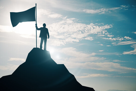 Person holding a flag on top of a mountain peak silhouetted against the sky, symbolizing victory and achievement