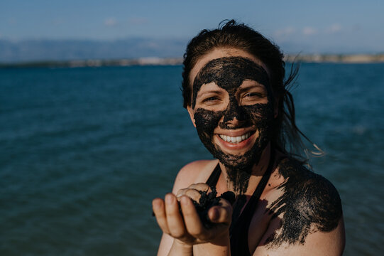 Woman applies healing mud to her face and body. Natural healing mud in Croatia on the beach.