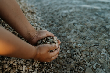 Close up of sea pebbles in boy's palms, pruney fingers. Seraching for shells in the sand. Concept of summer vacation by sea.