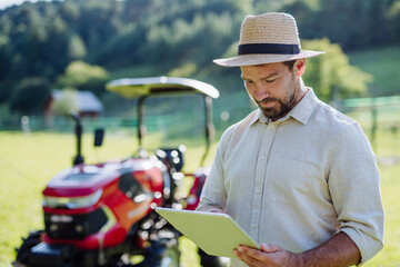 Farmer reading document in front of tractor on field. Grants, loans, funding opportunities for...
