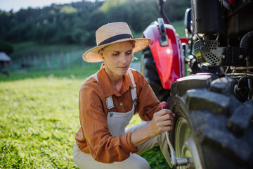Female farmer fixing a wheel on a tractor. Progressive farmer working on tractor on her own farm....