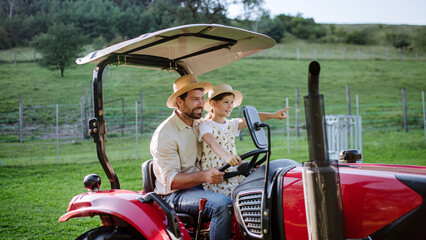 Farmer father riding tractor with his daughter. Girl growing up on family farm. Concept of multigenerational farming.