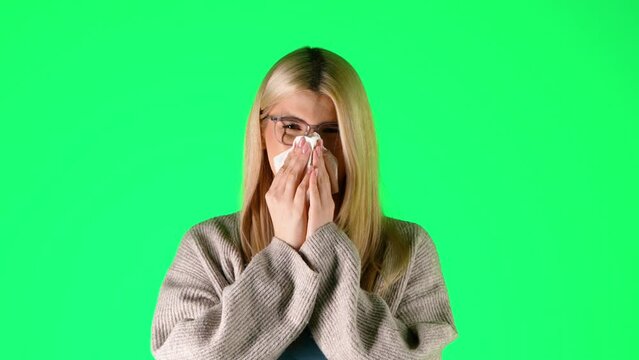 Caucasian Blonde Woman sneezes and blows her nose feeling sick, young studio chroma green background portrait shot