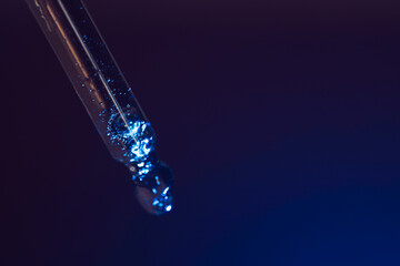 Skin care serum flows from a pipette under blue light