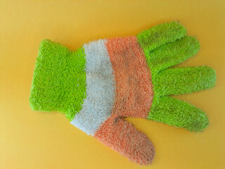 One glove made from dirty knitted wool for women with a dominant color of green, isolated on yellow background.