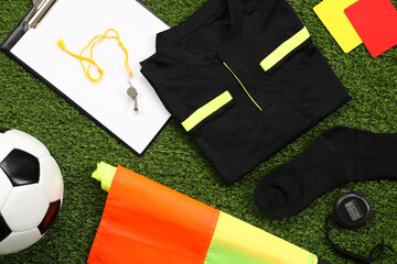 Uniform, soccer ball and other referee equipment on green grass, flat lay