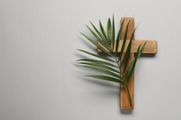 Wooden cross and palm leaf on light grey background, top view with space for text. Easter attributes