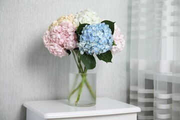 Beautiful hydrangea flowers in vase on white bedside table indoors