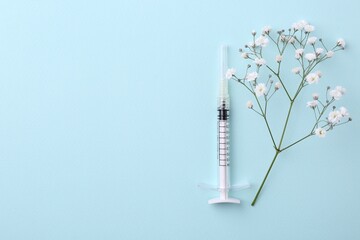 Cosmetology. Medical syringe and gypsophila on light blue background, flat lay. Space for text