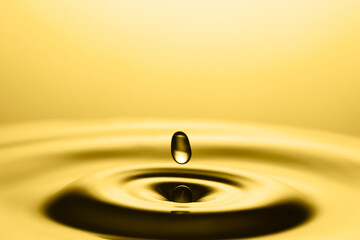 Splash of golden oily liquid with drop on yellow background, closeup