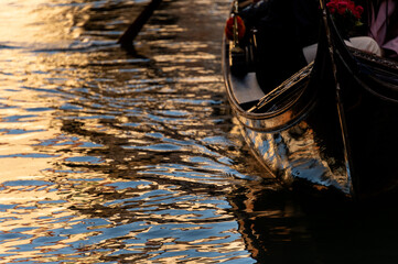 Symbolbild für Wenig Reisen, Morgensonne spiegelt sich im Kanal und reflektiert auf dem glatten schwarzen Rumpf einer Gondel. - obrazy, fototapety, plakaty
