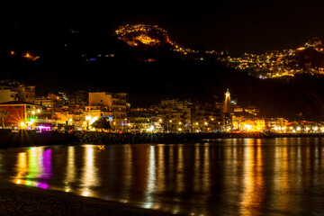 Fototapeta na wymiar night town coast with flashlights from embarkment and reflection in sea gulf water with golden urbal lights on background of landscape