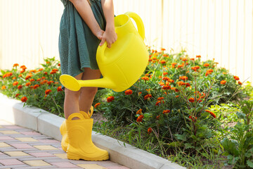 Close up child girl feet in yellow rubber boots standing in autumn or summer garden and watering...
