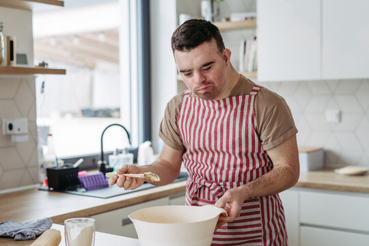 Young man with Down syndrome baking cookies at home. Everyday routine for man with Down syndrome.