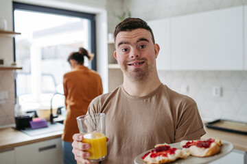 Young man with Down syndrome holding breakfast and glass of juice. Morning routine for man with...
