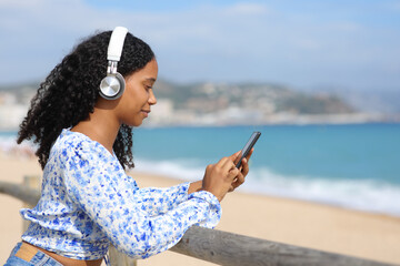 Black woman wearing headphone using phone on the beach - 745650501