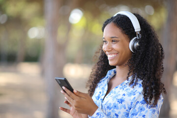Happy black woman listening music holding phone outside