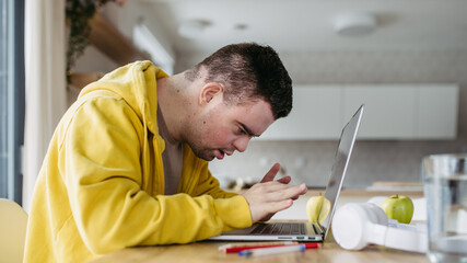 Young man with down syndrome learning online at home, using laptop. Telehealth consultation with...