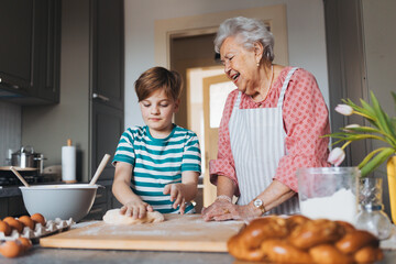 Grandmother with grandson preparing traditional easter meals, kneading dough for easter cross buns....