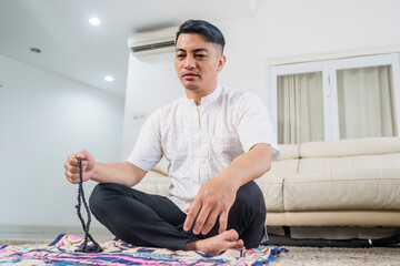 Close up of muslim man sitting on prayer rugs while holding beads to dhikr