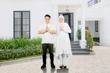 Muslim family of two adults showing greetings gesture in front of house © Creativa Images