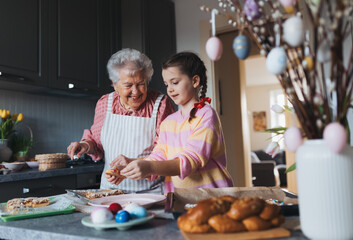 Grandmother with grandaughter preparing traditional easter meals, baking cakes and sweets. Passing...
