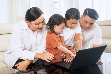 Asian family using laptop together in a living room at home