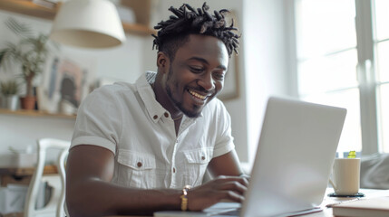 A joyful young man with dreadlocks works on a laptop in a bright, cozy room - obrazy, fototapety, plakaty