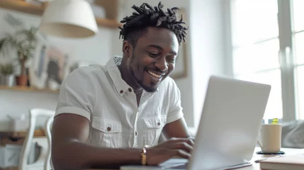 Foto op Canvas A joyful young man with dreadlocks works on a laptop in a bright, cozy room © ChubbyCat