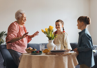 Grandmother with grandchildren setting table for traditional easter lunch. Recreating family traditions and customs.