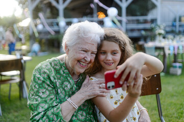 Young girl taking selfie with elderly grandmother at garden party. Love and closeness between...