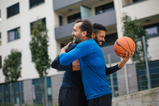 Best friends playing sport outdoors, having fun, hugging after game. Playing basketball at a local court, enjoying exercise together. Concept of male friendship, bromance.