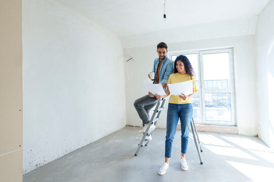 Happy couple discussing over blueprint in new home - Powered by Adobe