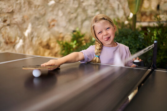 Playful girl sticking out tongue holding table tennis racket at villa