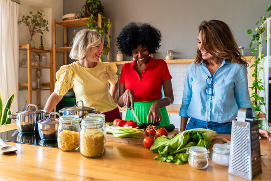 Woman cutting vegetables with friends in kitchen at home