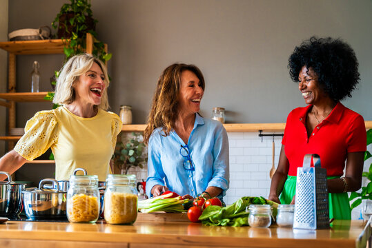 Happy women preparing food and laughing in kitchen at home