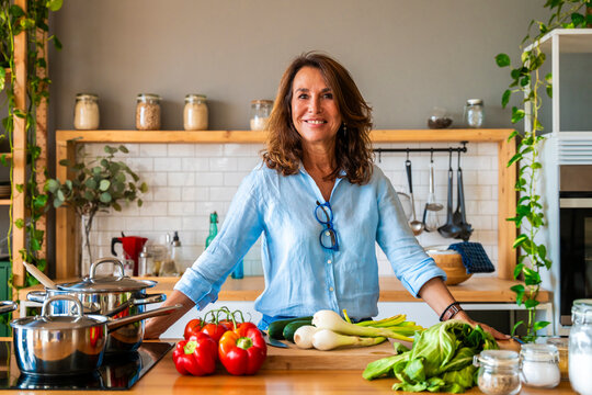 Smiling senior woman standing by vegetable on kitchen counter at home