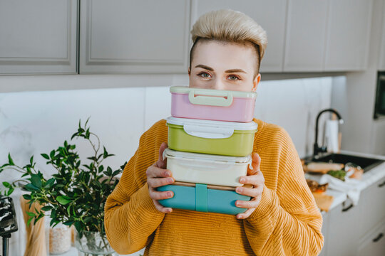 Young woman holding lunch boxes in kitchen at home