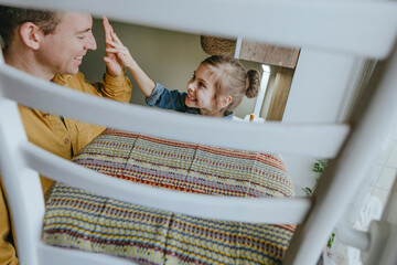 Happy father and daughter giving high-five near chair at home