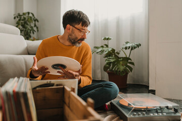Man holding vinyl looking at record player in living room