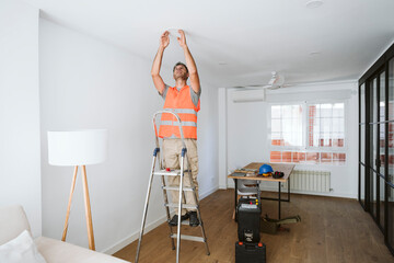 Repairman standing on ladder and working at home