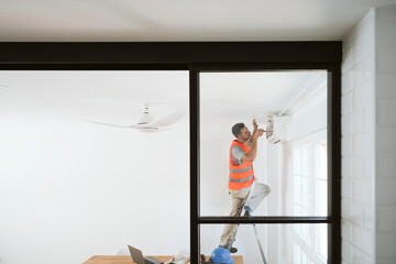 Mature technician fixing air conditioner in house under renovation