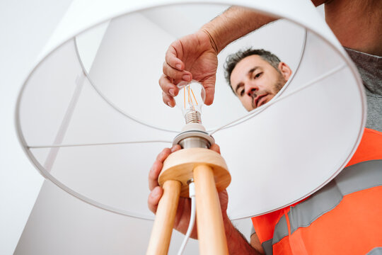 Electrician installing light bulb in lamp shade at home